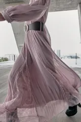 Vestido midi de color rosado con escote en pico y mangas largas. Presenta un diseño combinado con paneles de encaje en el frente y cierre frontal con botones forrados. Incluye un cinturón de cuero sintético marrón con hebilla metálica dorada.