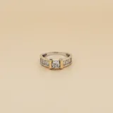Anillo de plata 925 con baño de oro, presenta un diseño con una piedra central de circonia redonda flanqueada por dos barras doradas y engaste de circonias baguette en los laterales.