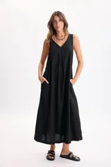 Vestido largo negro sin mangas, con escote en V, pinzas frontales, bolsillos laterales y caída fluida.