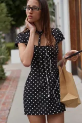 Vestido corto negro con estampado de lunares blancos, cuello redondo con lazada y escote cuadrado. Cuenta con mangas cortas y cierre trasero con cremallera oculta.
