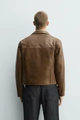 Cazadora de corte cropped confeccionada en piel con acabado napado. Presenta cuello solapa, cierre frontal con cremallera, manga larga y bolsillos de plastrón con solapa en el pecho. Destaca por sus pespuntes decorativos en contraste en toda la prenda.