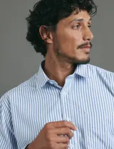 Camisa de vestir de manga larga con diseño de rayas verticales en tonos blanco y celeste. Presenta cuello clásico, cierre frontal con botones y un bolsillo en el pecho.