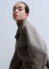 Chaqueta estilo overshirt de paño color gris, con cuello solapa, cierre frontal de botones oscuros, bolsillos con solapa en el pecho y bolsillos aplicados en la parte inferior.