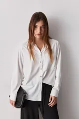 Camisa celeste de calce relajado, con cuello camisero, bolsillo aplicado en el pecho y mangas largas con puños abotonados. Cuenta con lazos ajustables en los laterales para fruncir y regular la silueta.
