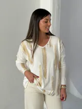 Sweater de punto con cuello en V y mangas largas, de diseño holgado. Presenta un estampado abstracto con pinceladas en color dorado sobre una base blanca.