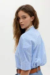 Camisa blanca de algodón con cuello mao, botonera oculta, mangas cortas estilo raglán con cortes estructurados y un bolsillo frontal con cierre.