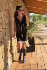 Vestido corto negro sin mangas, con escote en V y detalle de flecos en el ruedo. Presenta bordados en color blanco en el escote, los bolsillos y el centro del vestido.