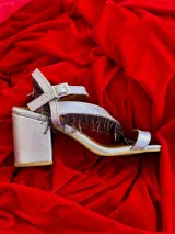 Sandalias de cuero marrón con tiras finas, cierre con hebilla y detalle de flecos con cuentas en el tobillo.