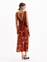 Vestido largo al tobillo confeccionado en seda de color rojo con estampado de limones y peras. Posee escote buche, diseño sin mangas, tajos laterales y detalle de tiras colgantes en el hombro.