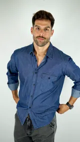 Camisa de denim azul de manga larga con cuello clásico, cierre frontal de botones y bolsillo en el pecho.