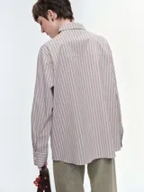 Camisa oversize de popelina de algodón con diseño de rayas verticales, cuello clásico, cierre frontal con botones, manga larga con puños anchos y bolsillo aplicado en el pecho.