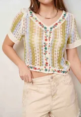 Blusa tejida de manga corta con diseño de rayas en tonos beige, verde y celeste, escote en V y detalles de bordado floral a lo largo de la botonadura y el ruedo.