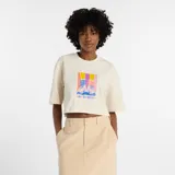 Remera corta de manga corta, color beige claro, con cuello redondo. Presenta un estampado frontal colorido que muestra un par de zapatillas con calcetines a rayas de colores vibrantes (amarillo, fucsia, azul) y el texto "new balance" debajo.