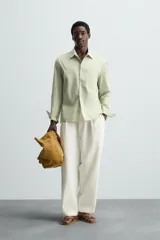 Camisa de hombre de corte relajado (relaxed fit) en color verde menta pálido, confeccionada en tejido con textura irregular acanalada. Presenta cuello solapa, manga larga con puño abotonado, bolsillo plastrón en el pecho y bajo asimétrico con aberturas laterales.