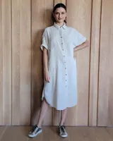 Túnica midi de lino con corte holgado, cuello camisero y cierre frontal completo con botones. Presenta mangas cortas con dobladillo y bolsillos laterales amplios.