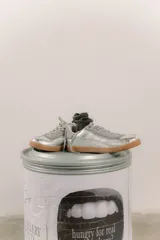 Zapatillas bajas de cuero color crema con detalles en marrón y cordones blancos.