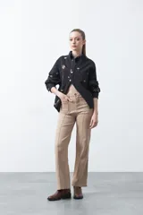 Pantalón de fit recto color beige, confeccionado en cotton spandex. Presenta costuras visibles y bordados decorativos en tono dorado/marrón claro. El ruedo del pantalón tiene un borde festoneado.