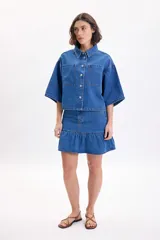 Falda corta de jean color azul medio, de tiro medio con diseño de volado en el ruedo.
