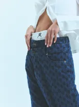 Jean de tiro bajo y corte oversize, confeccionado en denim azul con monograma grabado a láser en toda la prenda. Presenta doble botón metálico en la cintura y diseño de cinco bolsillos.