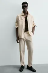 Pantalón chino de corte relajado, color beige claro, con textura de rayas verticales sutiles. Presenta cintura ajustable con cordón interior, bolsillos delanteros y bolsillos traseros de vivo.
