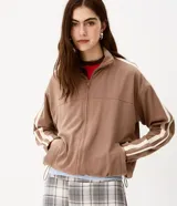 Campera deportiva oversized de microfibra color marrón, con cuello alto, cierre frontal y bolsillos laterales. Presenta bandas laterales contrastantes en las mangas y cordón ajustable en el dobladillo.