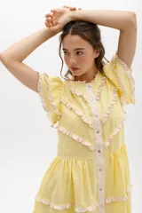 Vestido midi de lino blanco con diseño de broderie, cuello alto, cierre frontal con botones y volados decorativos en los hombros y el cuerpo.