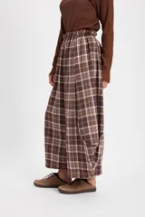 Pantalón de corte holgado con silueta tipo balloon, confeccionado en tela a cuadros. Presenta cintura elástica con cordón ajustable y cortes laterales circulares que aportan volumen a la prenda.