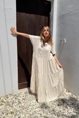 Vestido largo color beige, de lino, corte amplio, con cuello mao, mangas cortas y botones frontales. Tiene falda con volados escalonados.