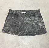 Mini falda de jean con efecto lavado ácido en tonos grises, de tiro bajo y corte recto. Presenta cierre frontal con botones y diseño de cintura asimétrica.