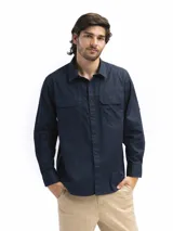 Camisa azul marino de manga larga confeccionada en algodón. Tiene cuello clásico, dos bolsillos frontales con tapa y velcro, abertura en la espalda con red interna y manga remangable con botón para fijar.