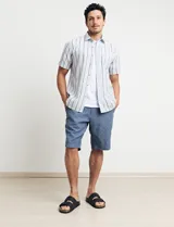 Camisa de manga corta con rayas verticales en tonos celeste, blanco, tostado y negro. Tiene cuello clásico, cierre con botones y bolsillo en el pecho.