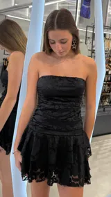 Vestido corto de encaje negro con diseño strapless, cuerpo drapeado y falda con volados en capas.