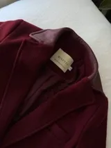 Tapado de lana color bordó con solapas y detalles en los bolsillos de cuero. Presenta cierre frontal con botones y diseño de líneas clásicas.