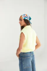 Camisa de lino color amarillo manteca, sin mangas, con cuello clásico y cierre frontal con botones. Presenta un diseño corto con nudo en el ruedo.