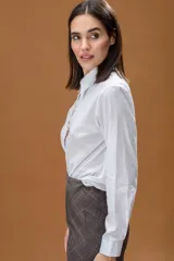 Camisa blanca de corte clásico, con cuello camisero, mangas largas con puños abotonados y cierre frontal con botones decorativos en forma de estrella con brillo.