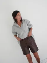 Bermuda de cuero color marrón oscuro con efecto desgastado, tiro medio, cierre frontal con botón y bolsillos.