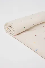 Pashmina de color crudo con estampado de pequeños puntos multicolores y flecos en los extremos. Cuenta con una etiqueta de cuero sintético con logo grabado.