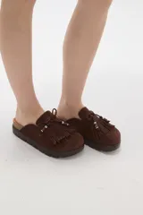 Suecos tipo mocasín color chocolate, confeccionados en material gamuzado. Presentan un diseño con flecos frontales, cordones decorativos con cuentas y una suela de plataforma plana de goma.