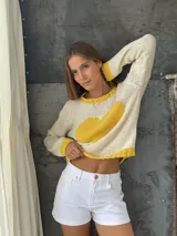 Buzo tejido a mano de lana merino, color crema con un diseño de corazón grande en color amarillo en el centro. Presenta cuello redondo, puños y ruedo acanalados en color amarillo.