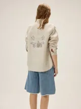 Camisa de lino color beige, de manga larga, con cuello camisero, pespuntes a contratono y estampa exclusiva en la espalda.