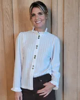 Camisa de manga larga con estampado de rayas verticales finas en color rosado sobre fondo blanco. Presenta cuello alto con volados, cierre frontal con doble botonadura y puños con volados.