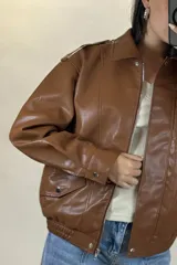 Chaqueta de ecocuero color marrón, de corte oversize, con cuello clásico, cierre frontal metálico, bolsillos laterales con solapa y puños con broches a presión.