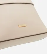 Cartera bandolera pequeña de material sintético color beige con detalles en marrón oscuro. Cuenta con cierre superior por cremallera, asa larga ajustable y placa metálica dorada con el logo de la marca en el frente.