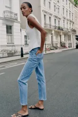 Jeans de tiro alto con diseño mom fit, tobilleros, de cinco bolsillos y cierre frontal con cremallera y botón, en color azul claro con efecto deslavado.