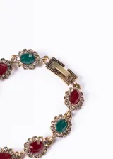Pulsera dorada con eslabones de bronce y cristales rojos, verdes y blancos engarzados en forma floral.