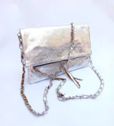 Cartera plateada tipo bandolera con solapa y cierre magnético. Tiene una cadena corta y una cadena larga.