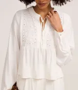 Blusa tipo bata de color celeste con mangas largas y cuello mao con lazo. Presenta detalles de bordado floral calado tipo laise en el frente y cierre parcial con botones.