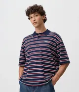 Remera polo de algodón con diseño a rayas horizontales en azul marino, rojo y blanco, corte boxy amplio, mangas cortas y cuello polo con botones. Presenta un pequeño bordado en el pecho.