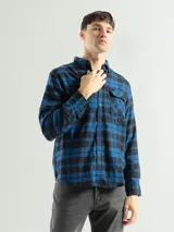 Camisa de franela a cuadros color celeste, gris y negro, de manga larga con dos bolsillos frontales con solapa abotonada.