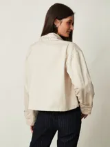 Campera cruda de gabardina con cierre frontal, bolsillos con cierre y cuello mao adornado con tachas plateadas.